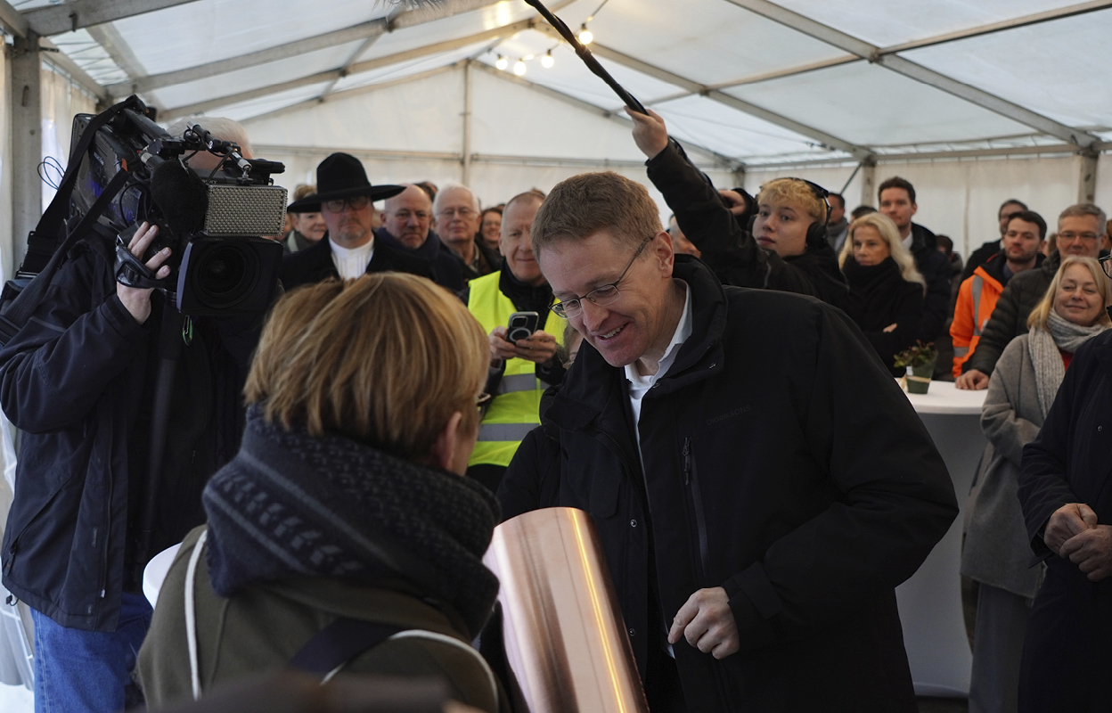 Ministerpräsident Daniel Günther befüllt die Zeitkapsel. Im Hintergrund sind Menschen zu sehen.